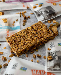 Unwrapped granola bar and some crumbs on a tile counter with other wrapped bars.